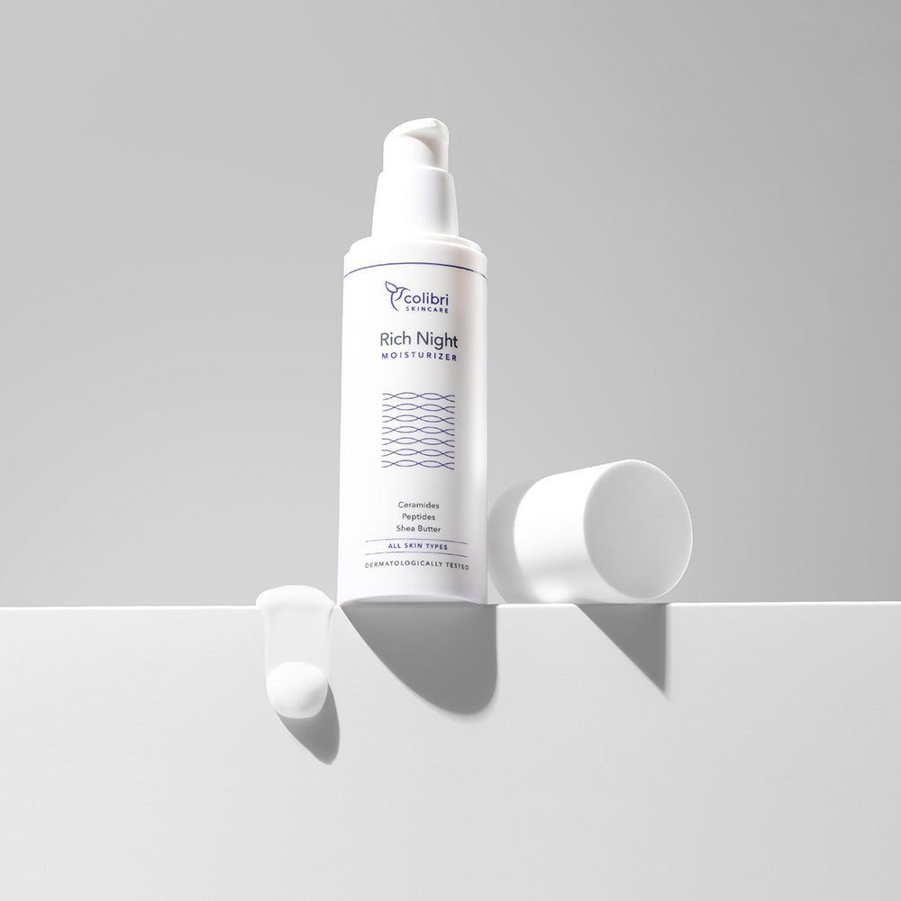 Eine Flasche "Rich Night Moisturizer" steht auf einem weißen Untergrund mit etwas Creme daneben.