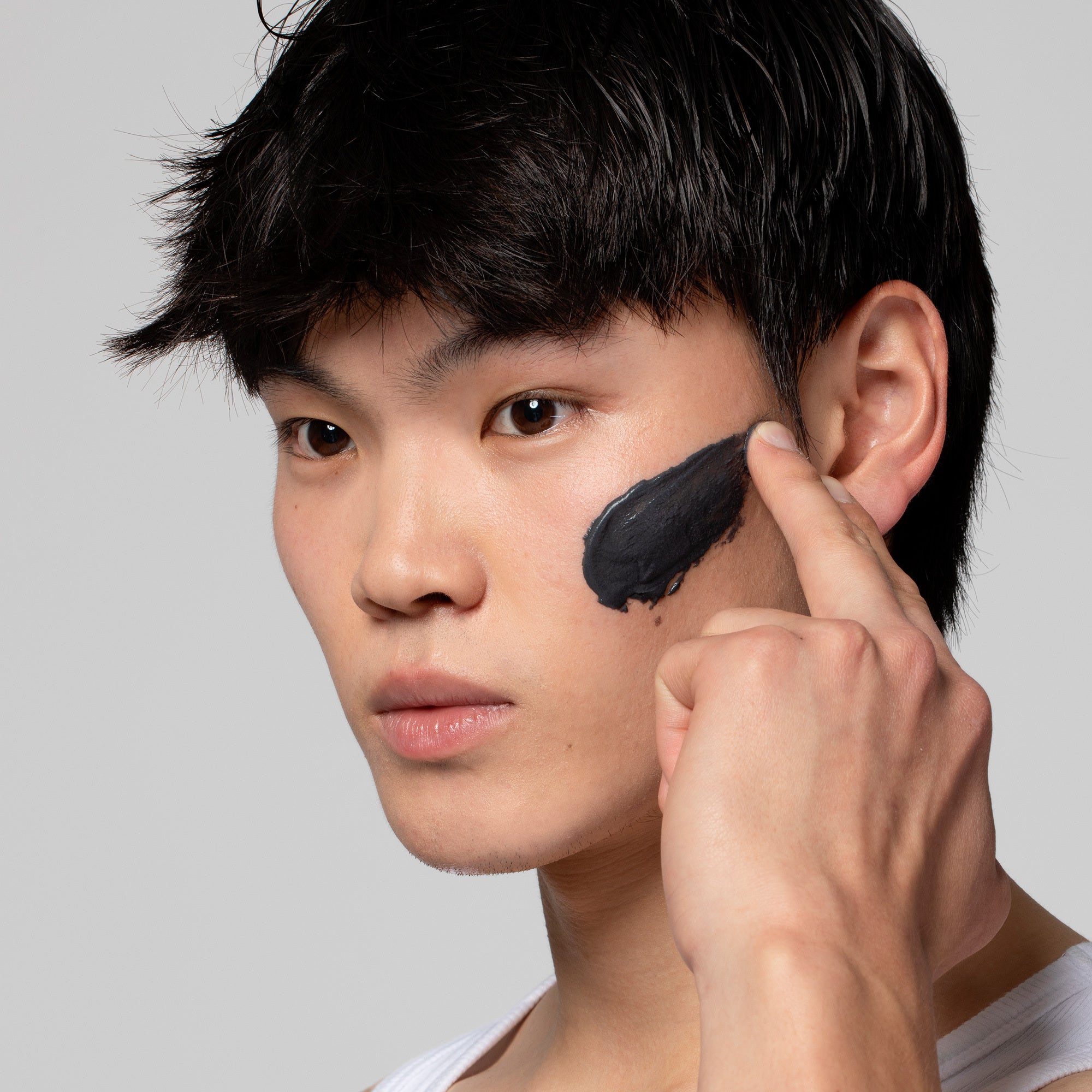 Ein junger Mann trägt schwarzen Gesichtsreiniger auf seine Wange auf.