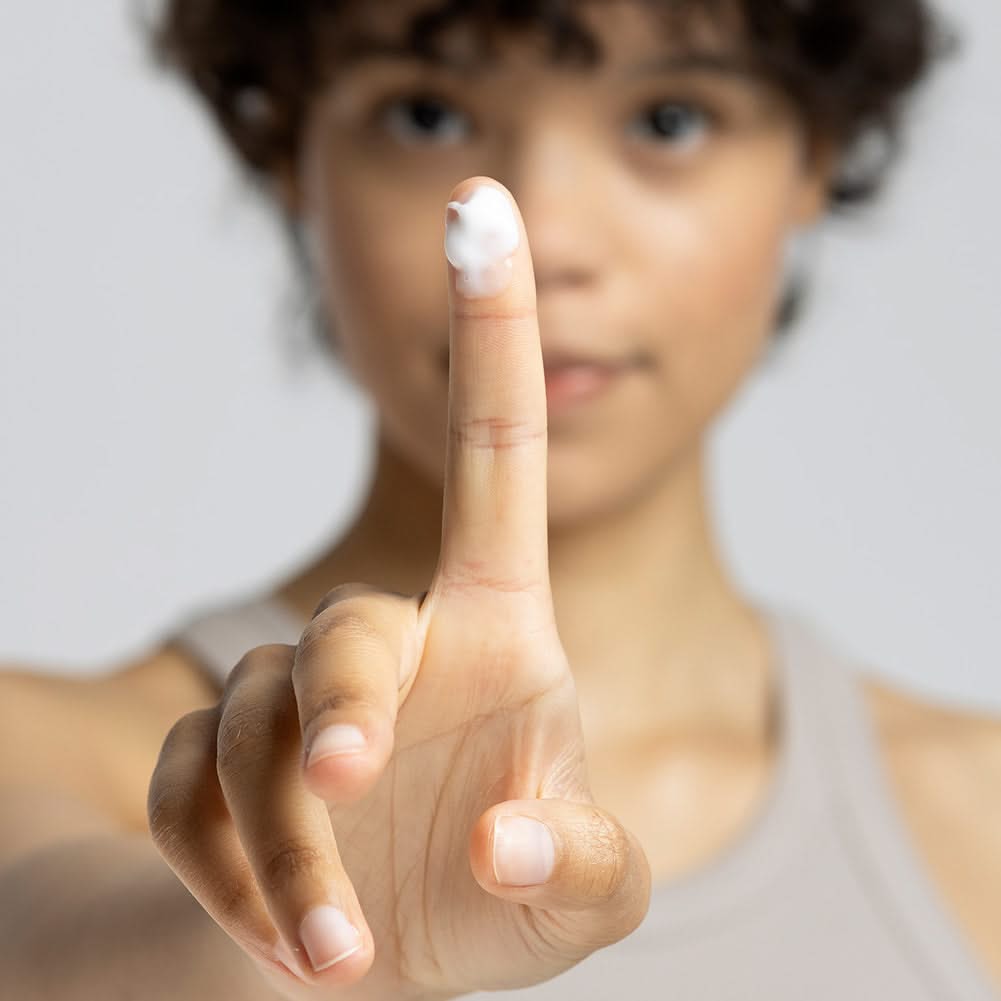 Person zeigt einen Finger mit einem Klecks Sahne oder Creme darauf.