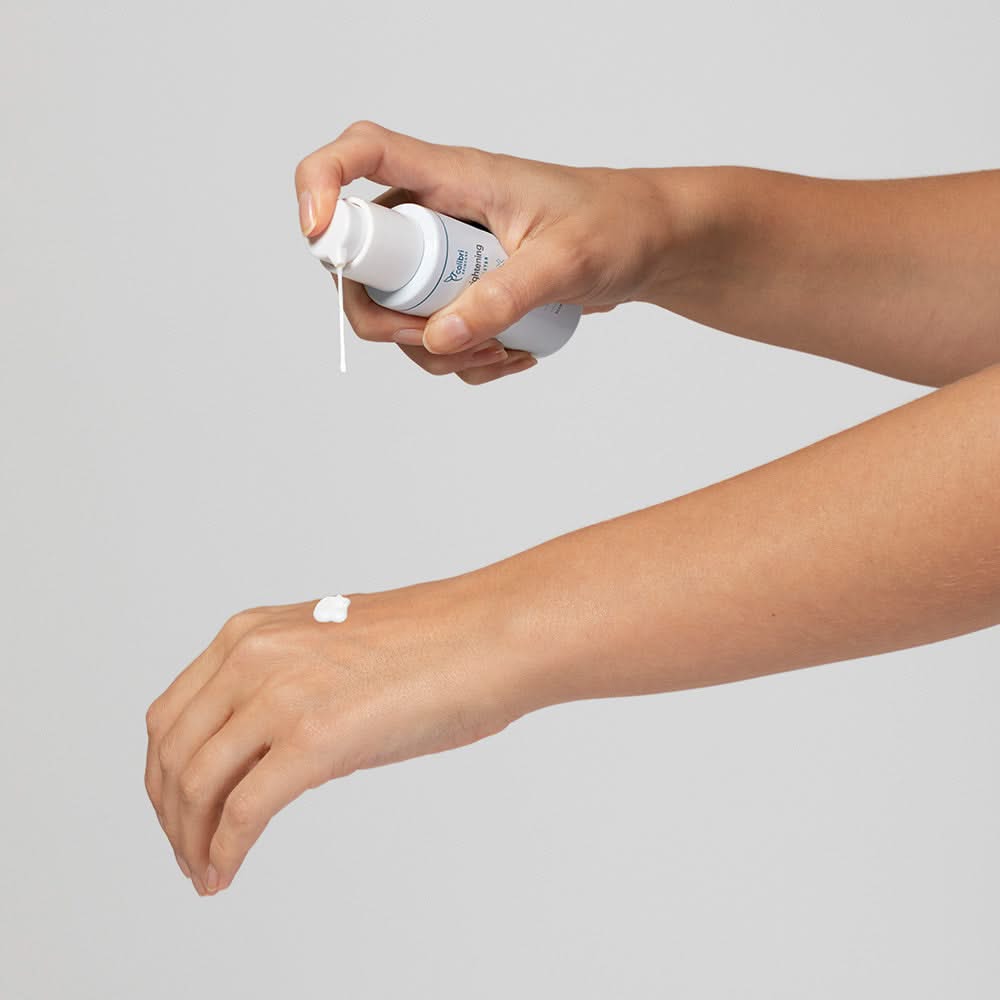 Eine Hand drückt Lotion aus einer Flasche auf den Handrücken der anderen Hand.