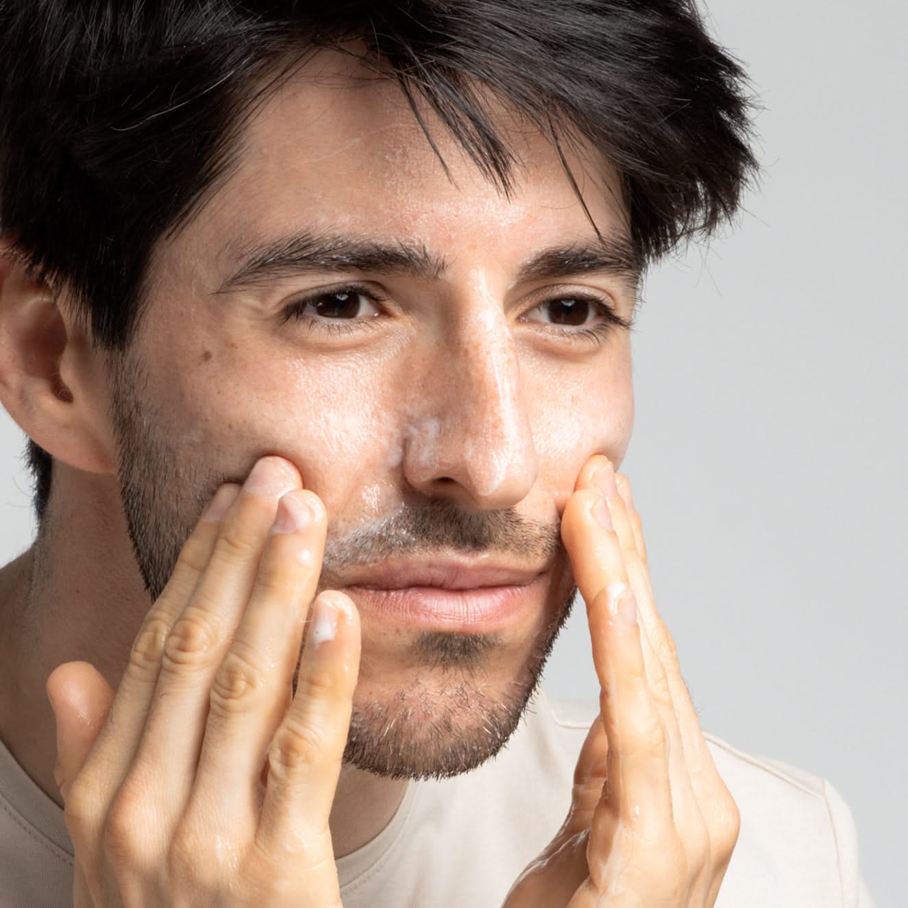 Ein Mann reinigt sein Gesicht mit Gesichtsreinigungsschaum und massiert sanft seine Wangen mit den Händen.