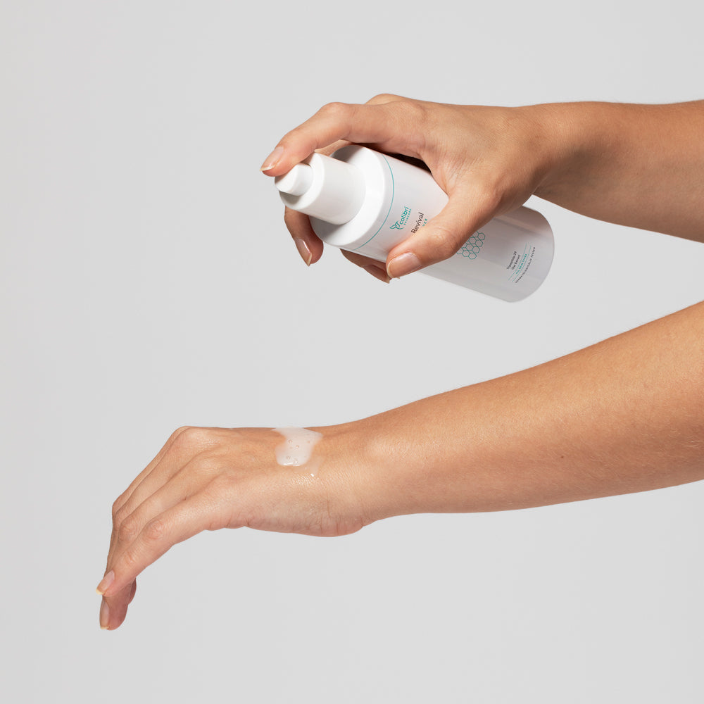 Eine Hand sprüht Flüssigkeit aus einer weißen Flasche auf den Unterarm einer anderen Hand.