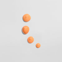Vier orange Farbtropfen auf einer weißen Oberfläche in einer absteigenden Anordnung.